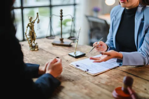 Lawyer consulting client at desk with legal documents, scales of justice, and gavel in office setting