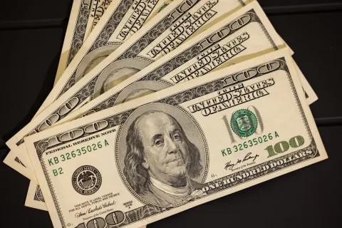 Fanned United States one hundred dollar bills showing Benjamin Franklin portrait and details.