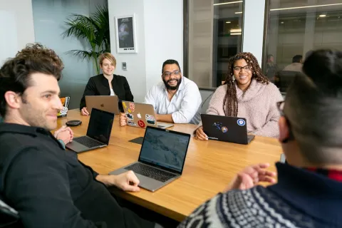 A diverse group of colleagues collaborating around a conference table with laptops in a modern office.