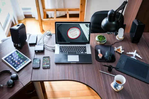 Modern workspace with laptop, tablet, smartphones, headphones, smartwatch, coffee cup, and desk accessories on a wooden table.