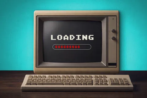 Vintage computer with loading screen showing dollar signs, set against a teal background on a wooden desk.