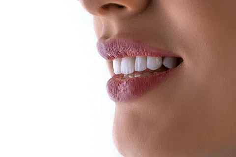 Close-up of a smiling woman’s mouth showing white teeth and natural pink lips against a white background