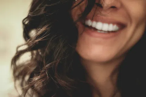 Close-up of a smiling woman with curly dark hair and bright white teeth.
