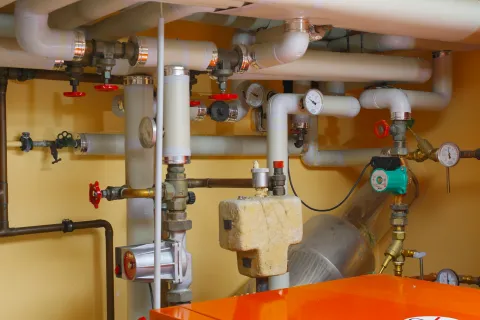 Complex plumbing setup with various valves, gauges, and pipes in a basement setting.