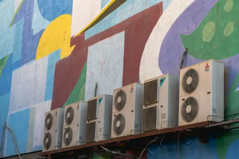 Row of outdoor air conditioning units against a colorful mural backdrop.