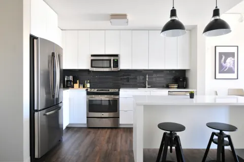 Modern kitchen with stainless steel appliances and sleek white cabinetry, featuring an island and stylish lighting.