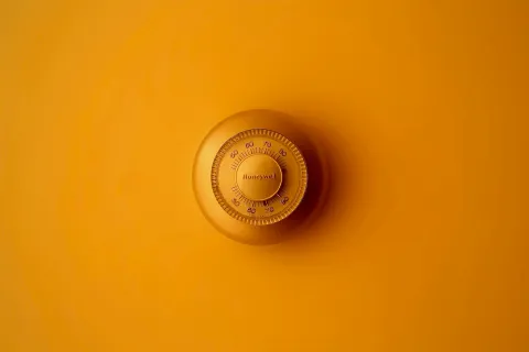 Honeywell thermostat against a vibrant orange background, highlighting its design and functionality.
