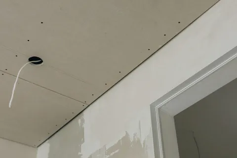Close-up of drywall installation showing electrical wire and unfinished wall surface.