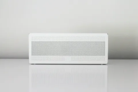 A sleek white Bluetooth speaker with a minimalistic design, placed on a reflective surface.