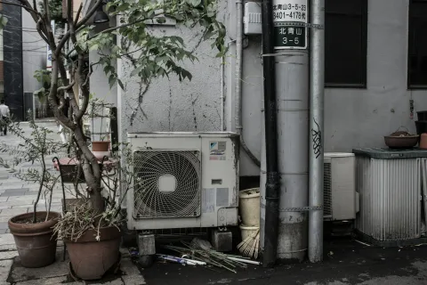 An outdoor scene featuring an air conditioning unit beside potted plants and utility poles.