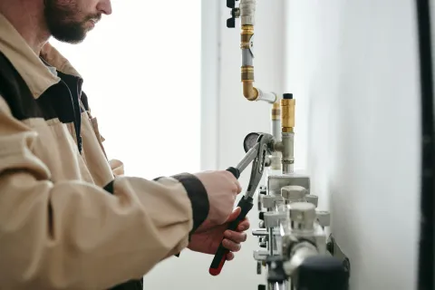 A man using a wrench to work on plumbing pipes in a well-lit setting.