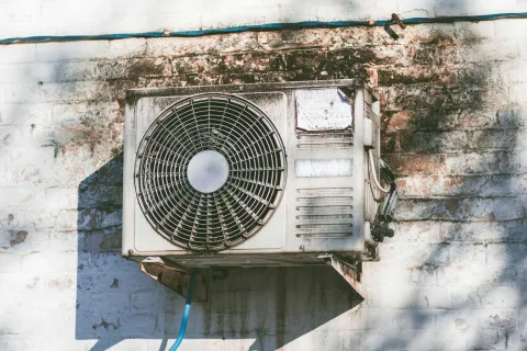 Old air conditioning unit mounted on a weathered brick wall with visible dirt and grime.