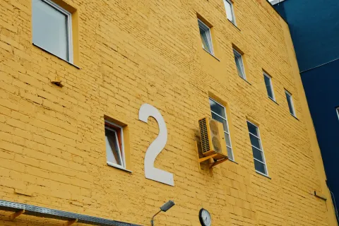 Bright yellow building wall featuring a large number 2 and windows, with an air conditioning unit visible.