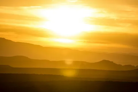 Golden sunset over mountains, casting warm light and shadows across the landscape.