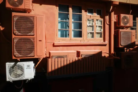 Colorful wall with various air conditioning units and a window casting shadows.