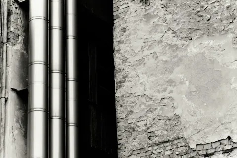 Industrial pipes against a textured, weathered wall in black and white.
