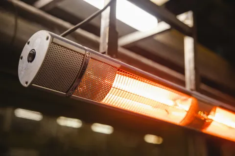 Illuminated infrared heating lamp hanging in an industrial setting, casting warm light.