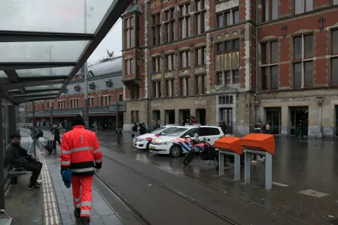 A busy street scene near a train station featuring police cars and pedestrians in rainy weather.