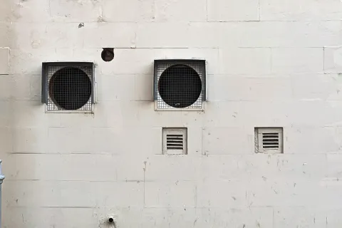 Two circular ventilation grates on a white wall, with smaller vents below them.