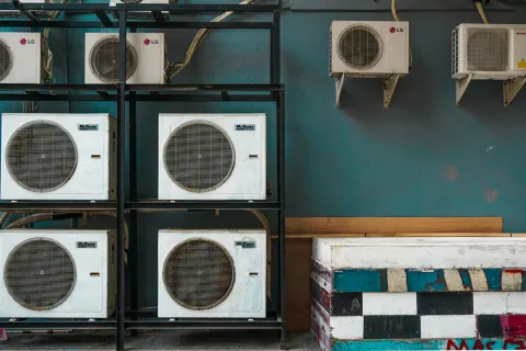 Array of air conditioning units mounted on wall with a blue background and colorful storage box below.