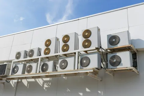 Multiple air conditioning units installed on a building exterior against a blue sky.
