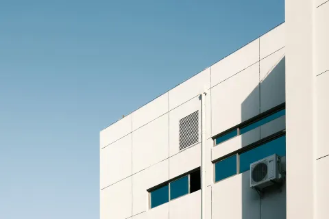 Modern building corner with windows and air conditioning unit against a clear blue sky.