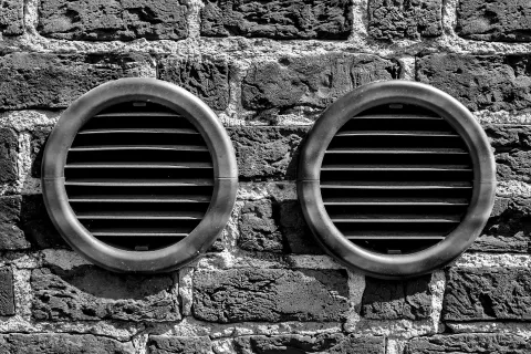 Two circular air vents on a textured stone wall in black and white.