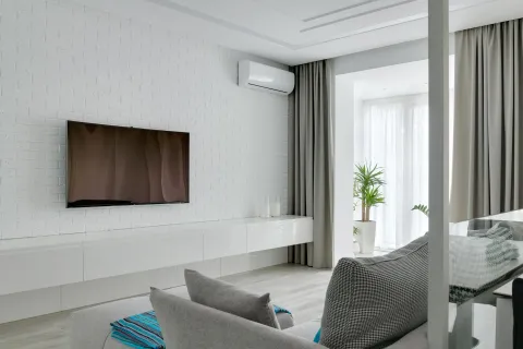 Modern living room featuring a wall-mounted TV, soft furnishings, and indoor plants in a light aesthetic.