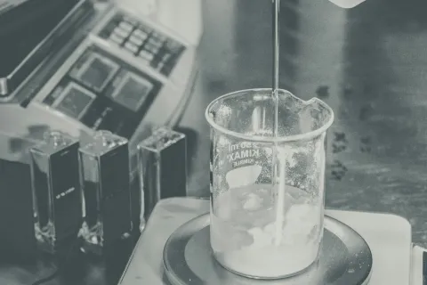 A laboratory scene showing a beaker being filled with liquid and scale equipment in the background.