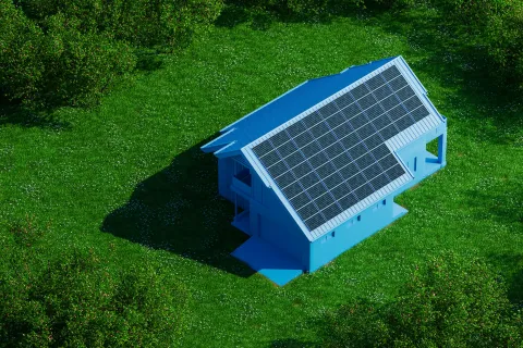 Blue house with large solar panels on the roof surrounded by grass and trees in bright daylight