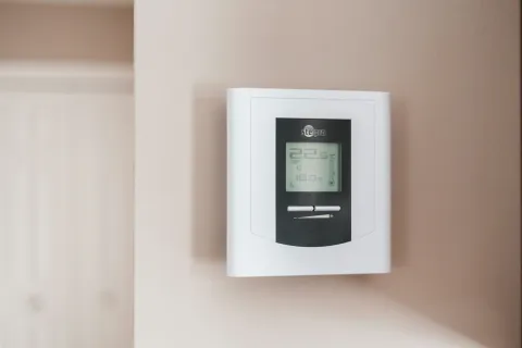Digital wall thermostat showing current temperature settings and controls on a beige wall indoors.
