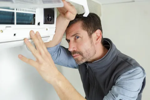 Technician inspecting and repairing a wall-mounted air conditioning unit indoors with focused attention.