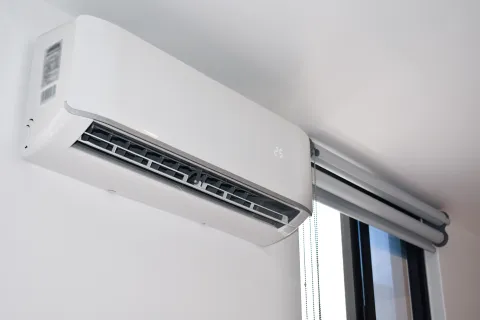 Modern split air conditioning unit mounted on a wall near a window, providing cooling options.