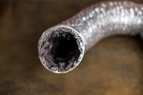 Close-up of a metal dryer vent hose clogged with lint and dust, emphasizing airflow blockage risk.