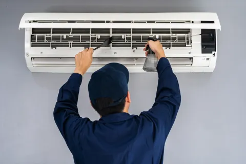 Technician cleaning an air conditioner unit for maintenance and efficiency.
