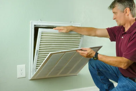 A man replacing an air filter in a home ventilation system.