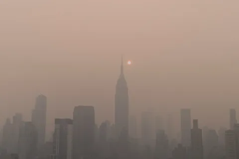 New York City skyline at sunset with skyscrapers silhouetted through thick haze or fog.