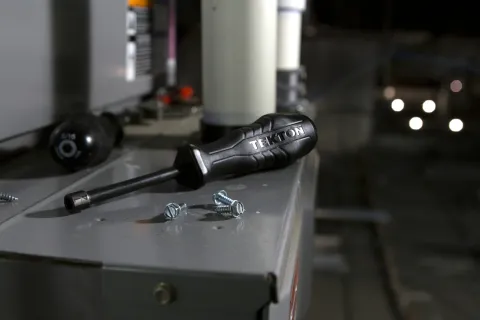 Tekton screwdriver and screws on a metal surface with blurred background and lighting bokeh.