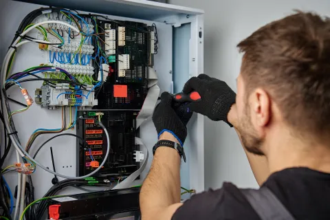 Technician working on electrical control panel with tools and wires in focus.