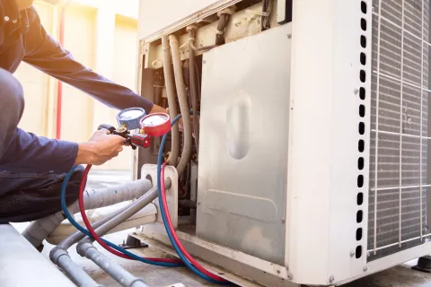 Technician using manifold gauge to check and service large air conditioning unit outdoors on sunny day