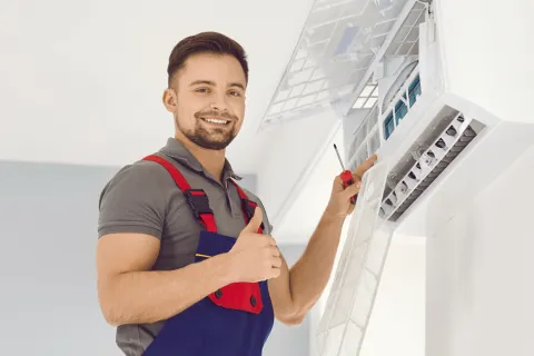 Smiling technician servicing an air conditioning unit with tools in hand, showcasing professionalism and expertise.