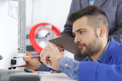Technician repairing equipment with a screwdriver in a workshop environment, focused and attentive to details.