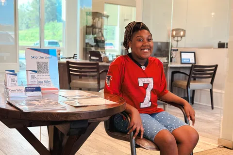 Smiling young woman in a red Atlanta Falcons jersey sitting on a chair in a modern office lobby.