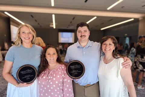 Four smiling people at an indoor event, two holding Paulding Chamber of Commerce awards, posing for a photo.