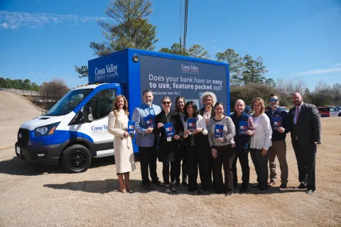 Group of people posing outdoors holding brochures in front of a Coosa Valley Credit Union branded van.