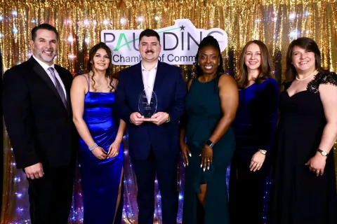 Group of six people dressed formally at an awards event with a gold sequin backdrop and Paulding Chamber of Commerce sign.