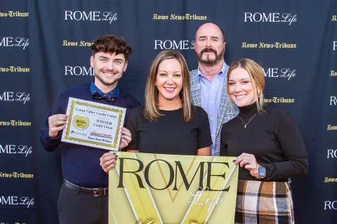 Joshua, Emily, Robert, and Paige holding Best of Rome 2025 winner banners on red carpet at Rome Life event for Coosa Valley Credit Union