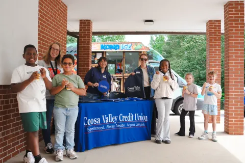 Group of children and adults enjoying drinks near Coosa Valley Credit Union booth and Kona Ice truck outdoors.