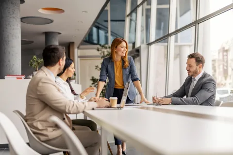 Business team in a modern office having a discussion around a white table by large windows during the day.