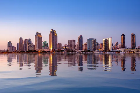 San Diego downtown skyline at dusk with buildings reflecting on calm bay waters under a clear sky.